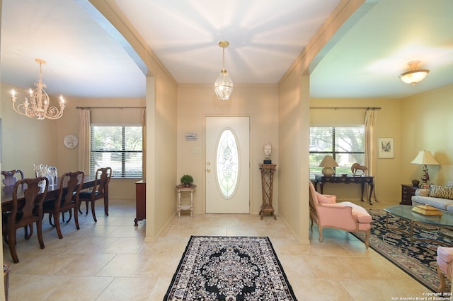 tiled foyer featuring ornamental molding, a healthy amount of sunlight, and an inviting chandelier