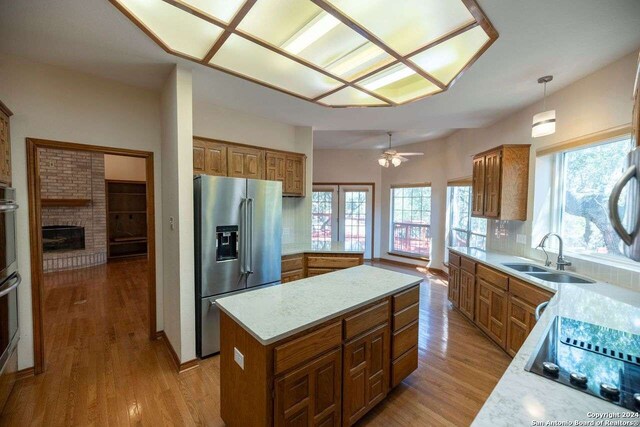 kitchen with stainless steel fridge, sink, ceiling fan, hanging light fixtures, and light hardwood / wood-style floors