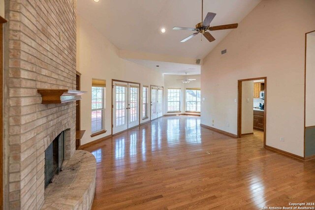 unfurnished living room with a fireplace, light hardwood / wood-style flooring, french doors, high vaulted ceiling, and ceiling fan