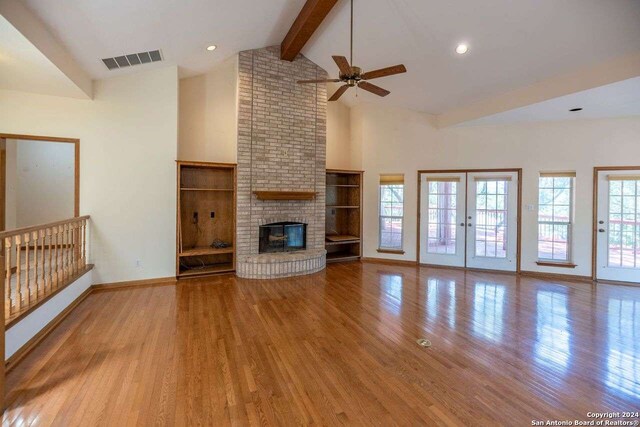 unfurnished living room featuring ceiling fan, a fireplace, vaulted ceiling with beams, and light hardwood / wood-style flooring