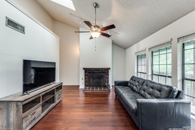 living room featuring dark wood-type flooring, vaulted ceiling with skylight, ceiling fan, and a textured ceiling