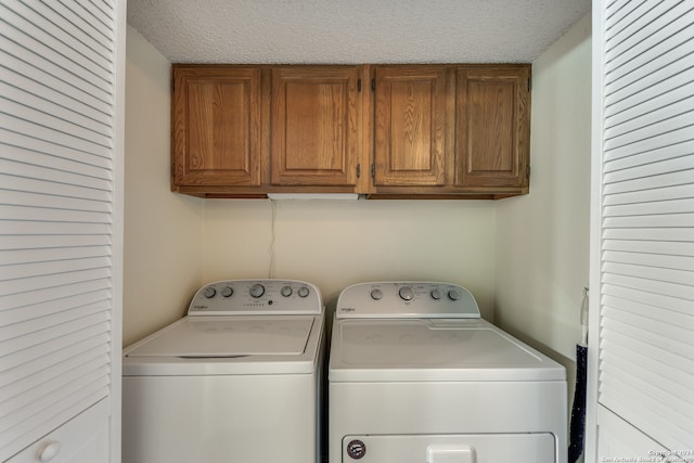 laundry area with washing machine and clothes dryer, cabinets, and a textured ceiling