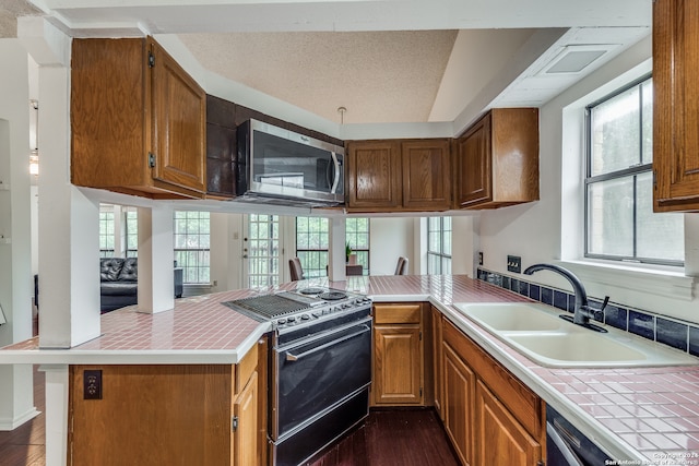 kitchen with black stove, dark wood-type flooring, kitchen peninsula, and sink