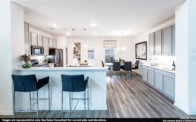 kitchen featuring decorative light fixtures, a breakfast bar, stainless steel appliances, kitchen peninsula, and light wood-type flooring