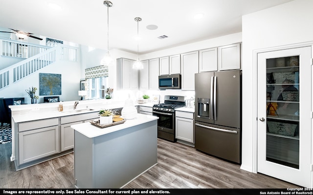 kitchen featuring gray cabinetry, decorative light fixtures, wood-type flooring, appliances with stainless steel finishes, and kitchen peninsula