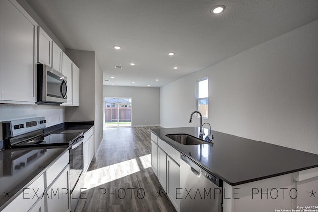 kitchen with dark wood-type flooring, sink, an island with sink, white cabinets, and appliances with stainless steel finishes