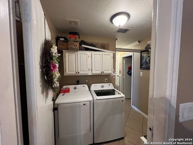 laundry area featuring light tile patterned floors, washing machine and clothes dryer, cabinets, and a textured ceiling