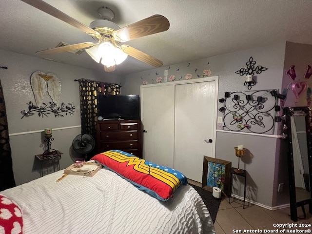 bedroom with a textured ceiling, light tile patterned flooring, ceiling fan, and a closet