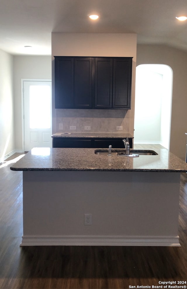 kitchen featuring stone countertops, sink, dark wood-type flooring, decorative backsplash, and a center island with sink