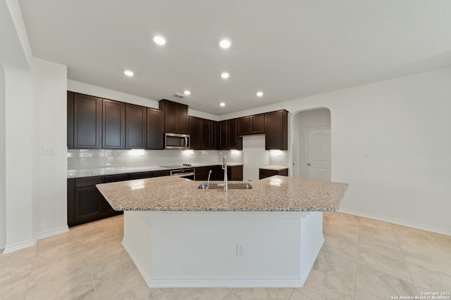 kitchen featuring a center island with sink, light stone counters, sink, and dark brown cabinets