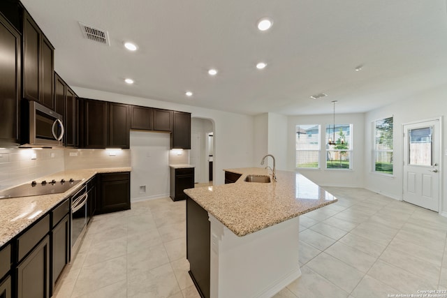 kitchen with pendant lighting, stainless steel appliances, light stone counters, sink, and a center island with sink