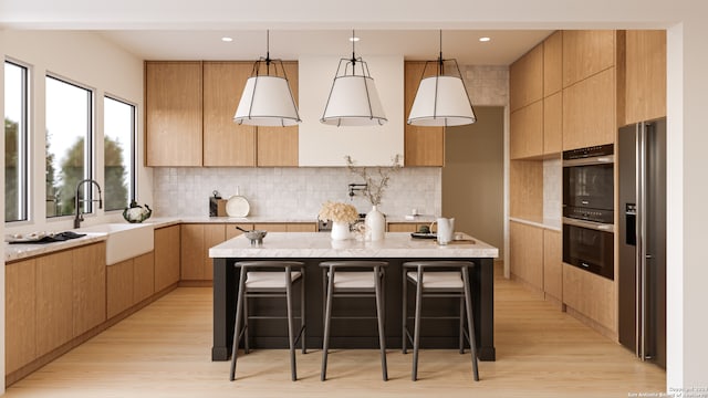 kitchen with stainless steel appliances, light hardwood / wood-style floors, a kitchen island, hanging light fixtures, and a breakfast bar area