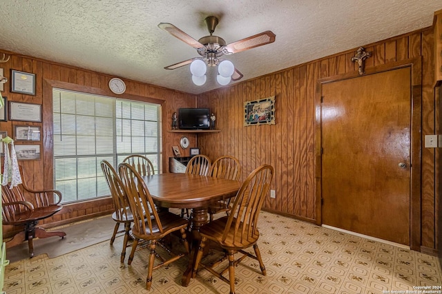 dining area featuring ceiling fan, a textured ceiling, and wood walls