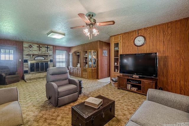 carpeted living room featuring ceiling fan, a stone fireplace, a textured ceiling, and a healthy amount of sunlight