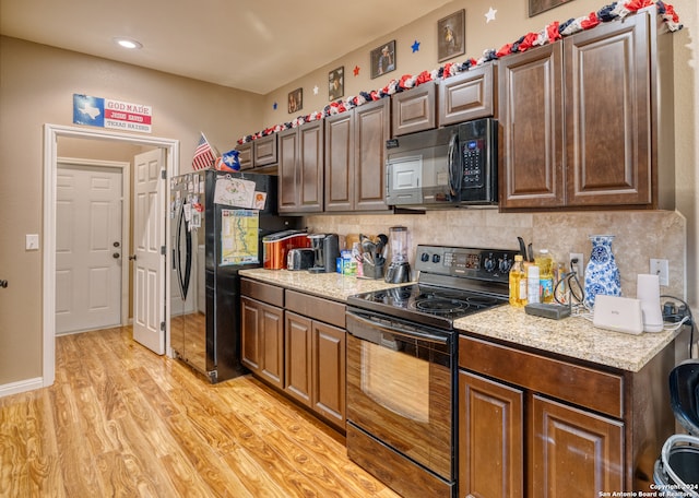 kitchen with light hardwood / wood-style floors, tasteful backsplash, light stone countertops, black appliances, and dark brown cabinetry