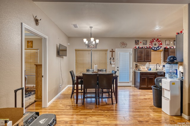 dining space with light wood-type flooring, an inviting chandelier, and sink