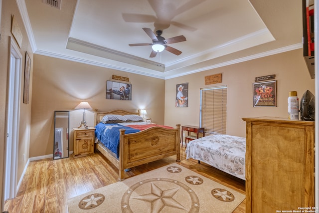 bedroom featuring light wood-type flooring, a tray ceiling, ceiling fan, and crown molding