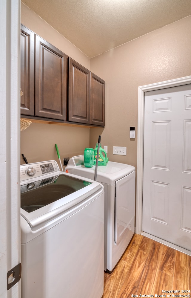 washroom featuring cabinets, light wood-type flooring, washer and dryer, and a textured ceiling