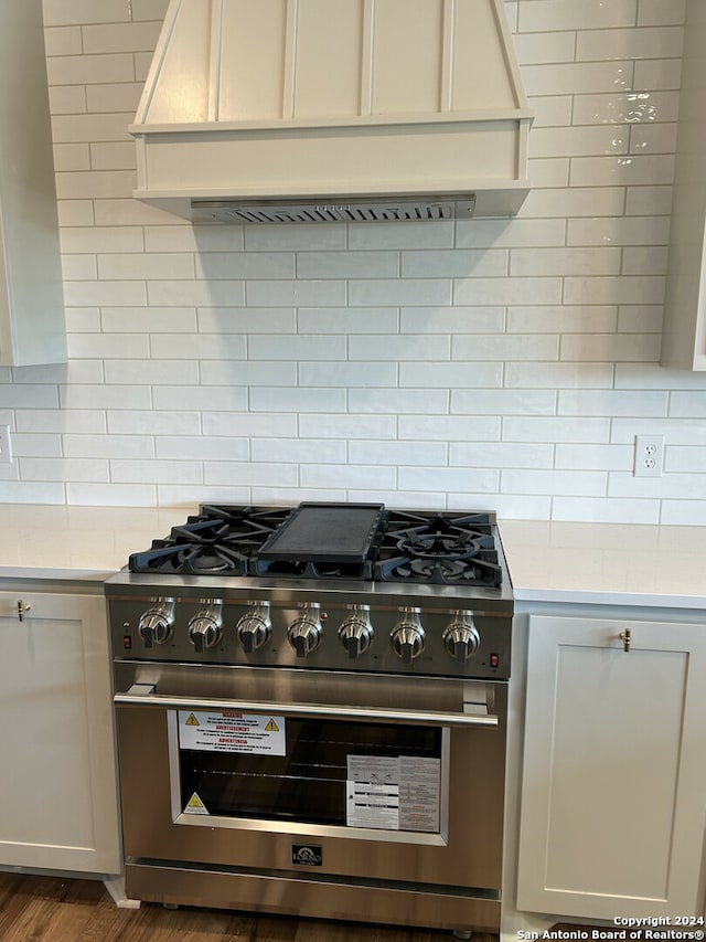 kitchen with backsplash, white cabinetry, custom range hood, stainless steel range, and dark hardwood / wood-style flooring