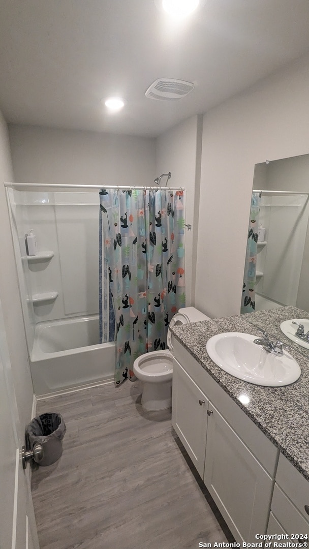 full bathroom with wood-type flooring, vanity, shower / bath combo with shower curtain, and toilet