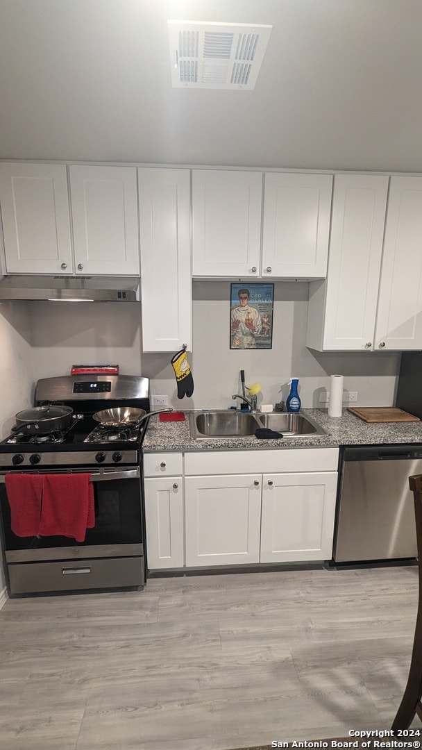 kitchen featuring white cabinetry, light stone countertops, stainless steel appliances, light hardwood / wood-style flooring, and sink