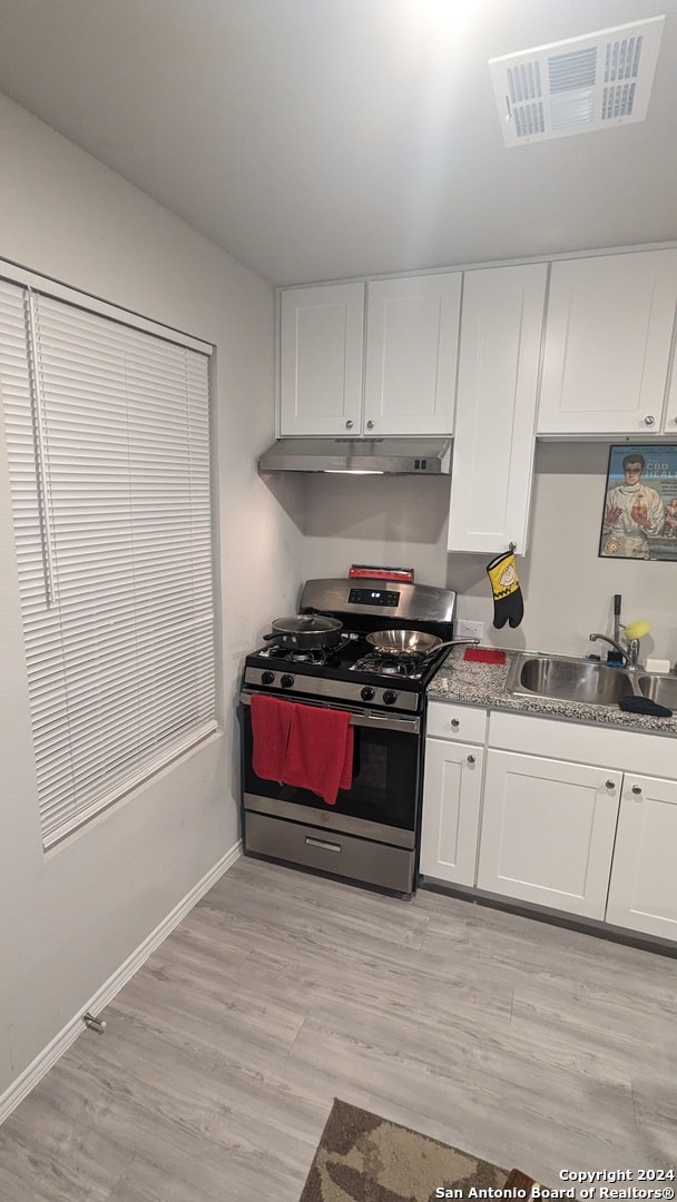 kitchen with light hardwood / wood-style flooring, white cabinets, gas stove, and sink