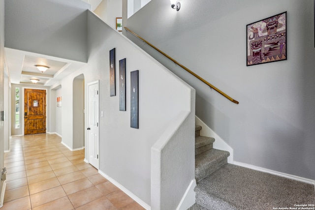 stairs featuring a raised ceiling and tile patterned floors