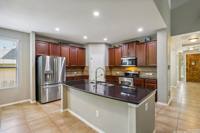 kitchen featuring backsplash, light tile patterned floors, stainless steel appliances, a center island with sink, and sink