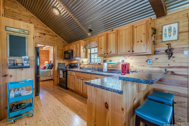 117 Hawk Rd, Fredericksburg, TX 78624 - kitchen featuring dark countertops, black appliances, a peninsula, light wood finished floors, and wood walls