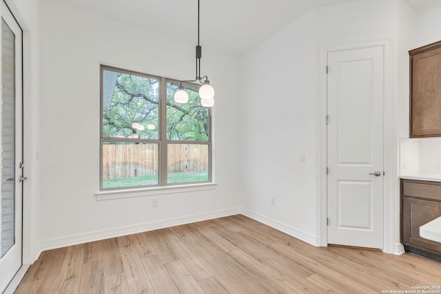 unfurnished dining area with a notable chandelier, light hardwood / wood-style floors, and lofted ceiling