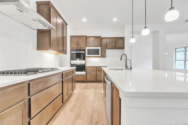 kitchen with pendant lighting, ventilation hood, sink, an island with sink, and stainless steel appliances