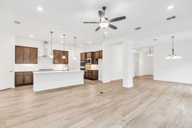 kitchen featuring a center island with sink, pendant lighting, and wall chimney range hood