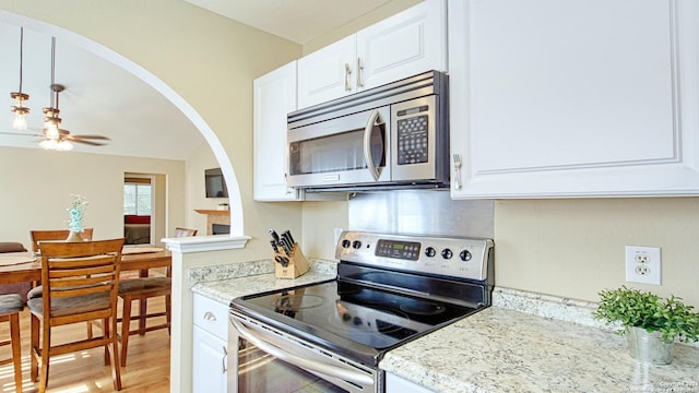 kitchen with light stone counters, light hardwood / wood-style floors, white cabinetry, stainless steel appliances, and ceiling fan