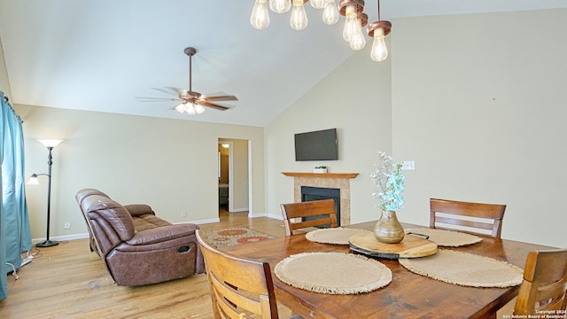 dining room with light hardwood / wood-style flooring, a tiled fireplace, high vaulted ceiling, and ceiling fan with notable chandelier