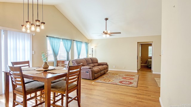 dining area featuring light wood-type flooring, ceiling fan with notable chandelier, and high vaulted ceiling