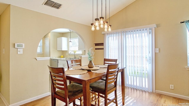 dining space featuring vaulted ceiling, an inviting chandelier, light hardwood / wood-style flooring, and sink