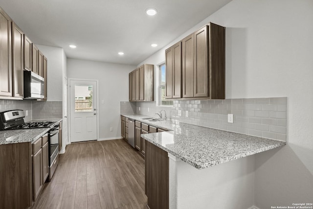 5103 Sandstone Way, San Antonio, TX 78222 - kitchen with appliances with stainless steel finishes, a peninsula, wood finished floors, light stone countertops, and tasteful backsplash
