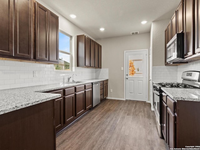 kitchen with dark brown cabinets, hardwood / wood-style flooring, stainless steel appliances, backsplash, and light stone countertops