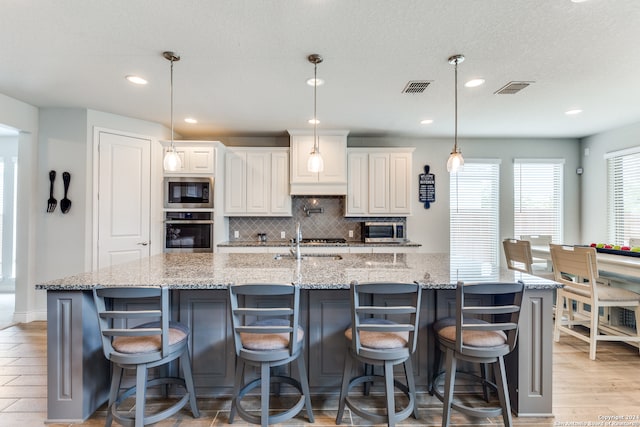 kitchen with light stone counters, decorative light fixtures, a large island with sink, appliances with stainless steel finishes, and a kitchen breakfast bar