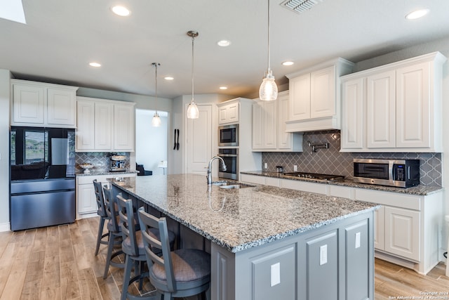 kitchen with white cabinets, an island with sink, stainless steel appliances, and light wood-type flooring