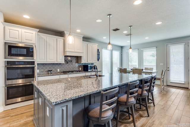 kitchen featuring light hardwood / wood-style flooring, white cabinets, light stone counters, and an island with sink