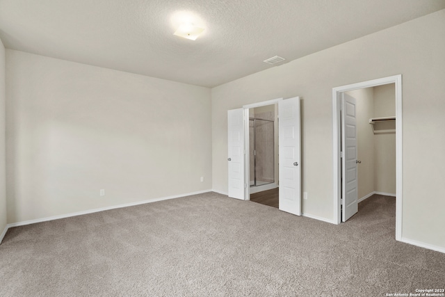 unfurnished bedroom featuring a textured ceiling, carpet, a closet, a spacious closet, and ensuite bathroom