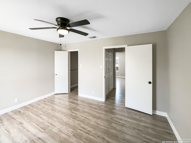 unfurnished bedroom with hardwood / wood-style floors, ceiling fan, a walk in closet, and a closet