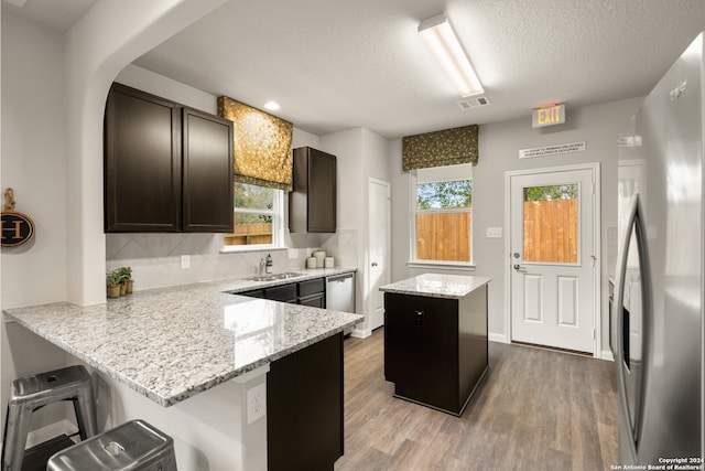 kitchen featuring appliances with stainless steel finishes, a breakfast bar, kitchen peninsula, a kitchen island, and light stone countertops