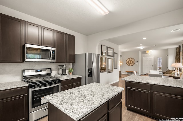 kitchen with backsplash, stainless steel appliances, a center island, light hardwood / wood-style flooring, and dark brown cabinetry