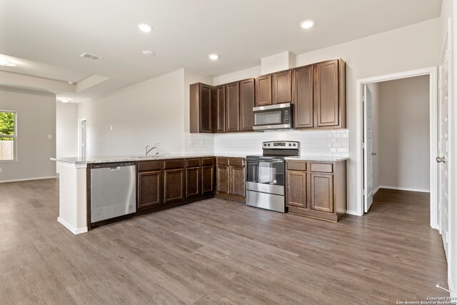 kitchen with kitchen peninsula, decorative backsplash, light wood-type flooring, light stone counters, and stainless steel appliances