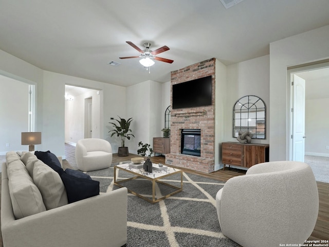 living room featuring a brick fireplace, wood-type flooring, and ceiling fan