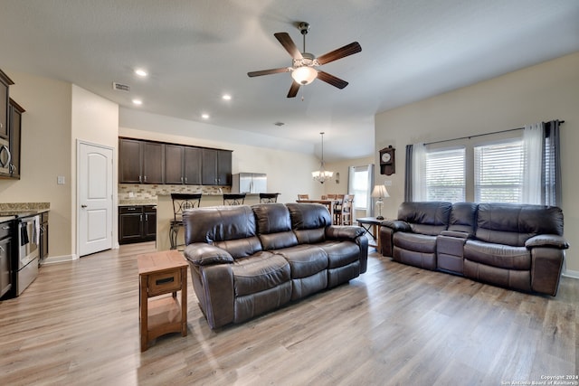 living room featuring ceiling fan with notable chandelier, light wood-type flooring, and a textured ceiling