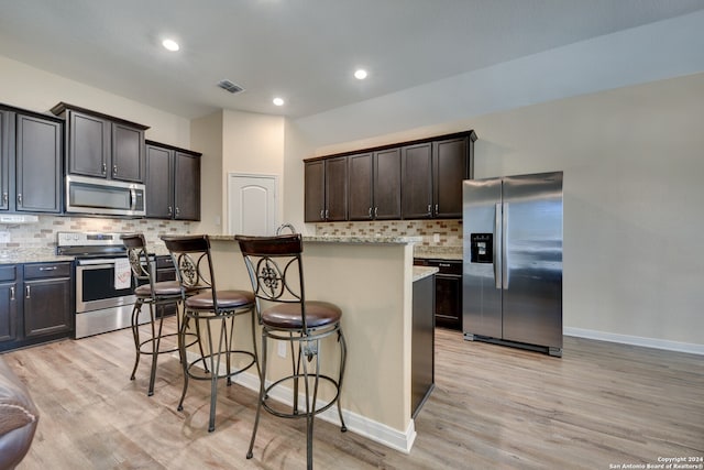 kitchen with dark brown cabinets, a kitchen island with sink, stainless steel appliances, and light hardwood / wood-style flooring