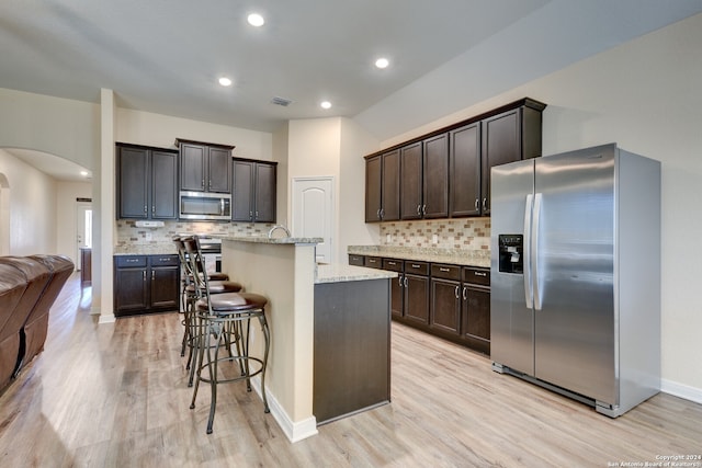 kitchen featuring a kitchen breakfast bar, stainless steel appliances, light hardwood / wood-style flooring, dark brown cabinetry, and a kitchen island with sink